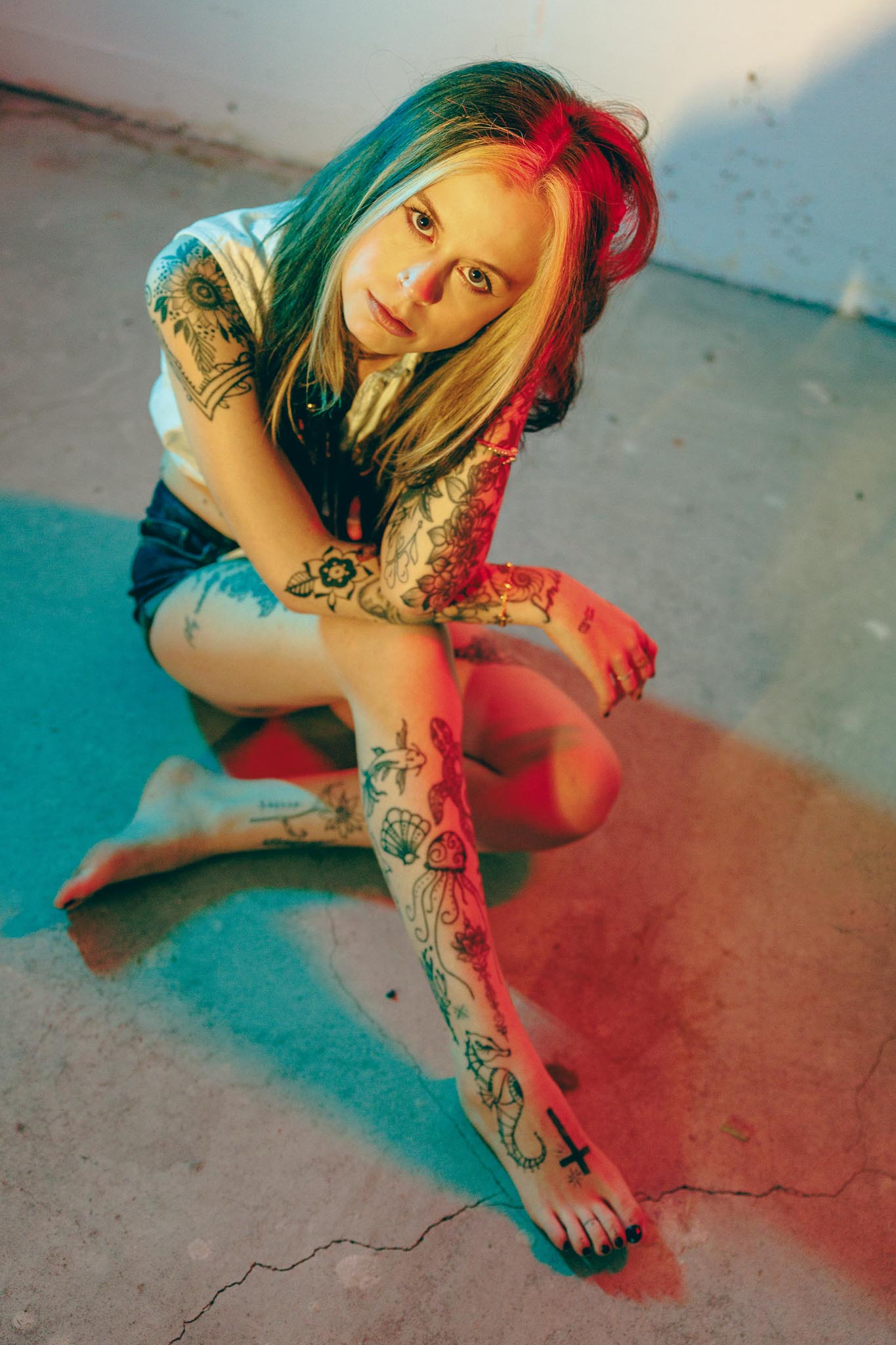 Juliana auf dem Betonboden, rotes und teal Gegenlicht, Tattoos